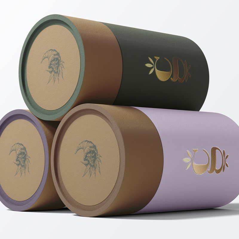 Custom cylindrical merchandise packaging design for Cornucopia Growers featuring textured paper tubes with premium foil branding and color-coded product variations.