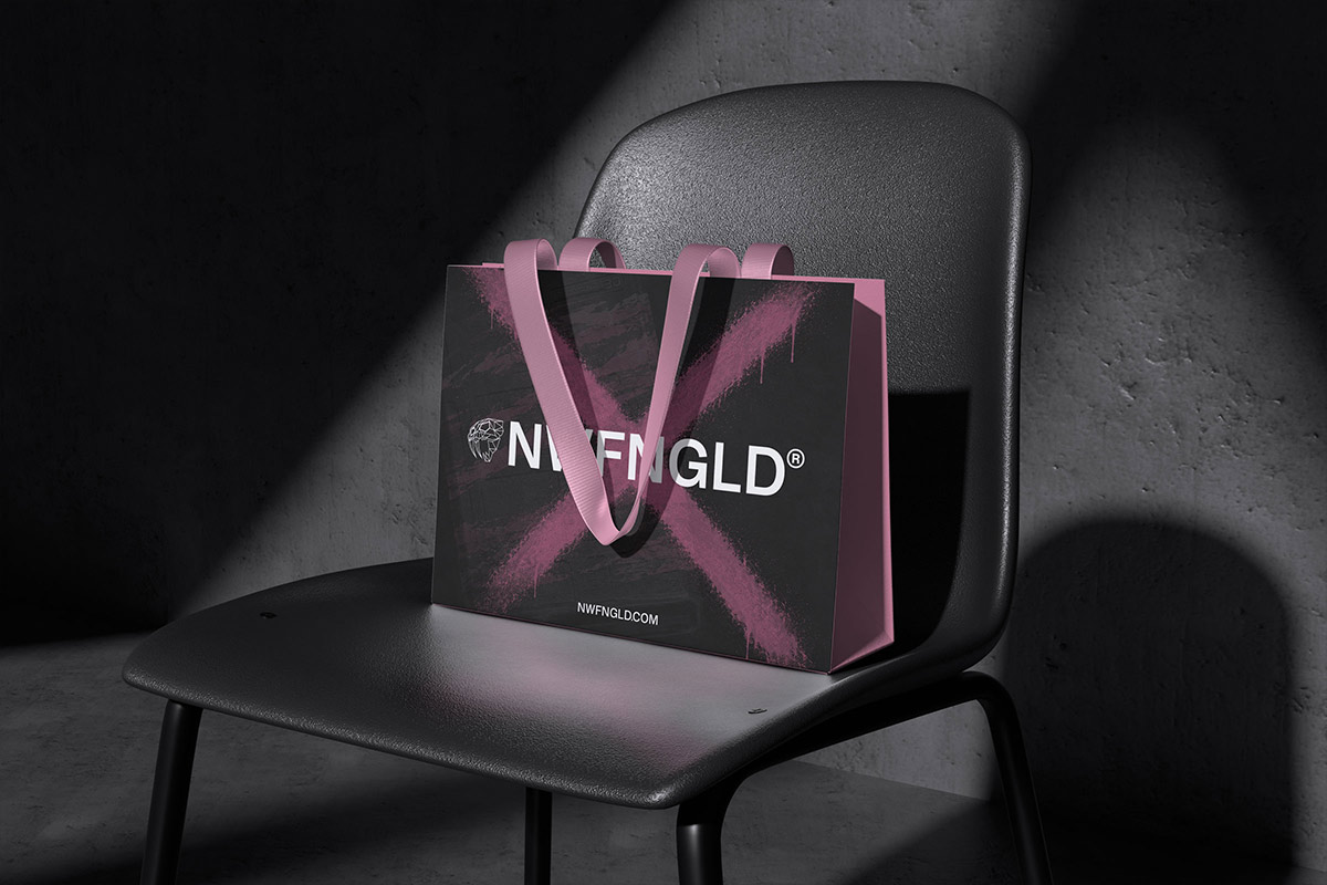 A black NWFNGLD shopping bag with pink handles and a pink spray-painted "X," resting on a dark chair in a concrete room with a shaft of light across it.