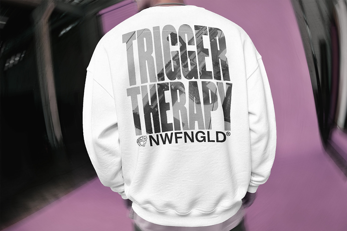 Back view of a white Newfangled Tactical crewneck sweatshirt with "Trigger Therapy" in photo-filled lettering above the NWFNGLD logo.