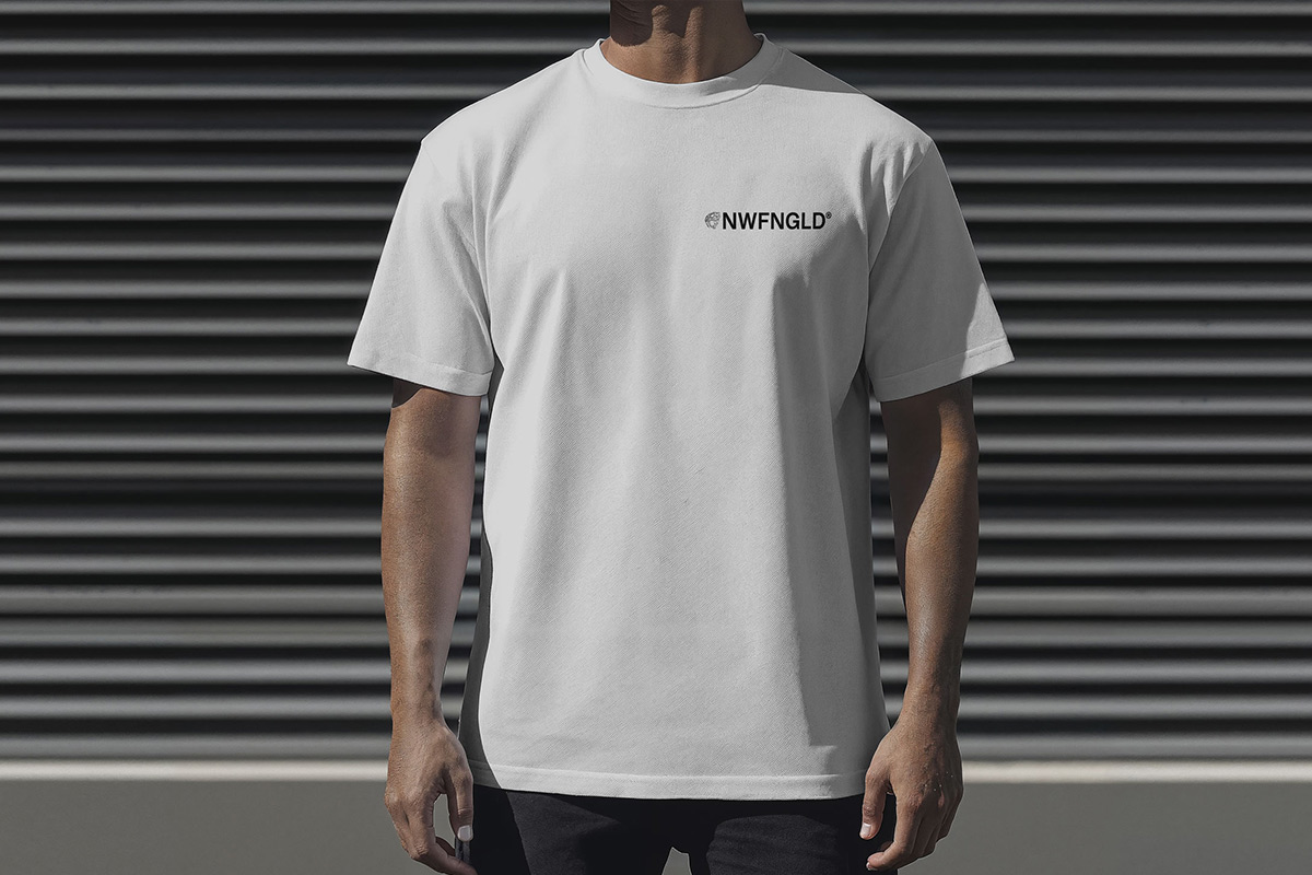 A man in a white oversized Newfangled Tactical tee with a small NWFNGLD chest logo, standing against a grey metal shutter.