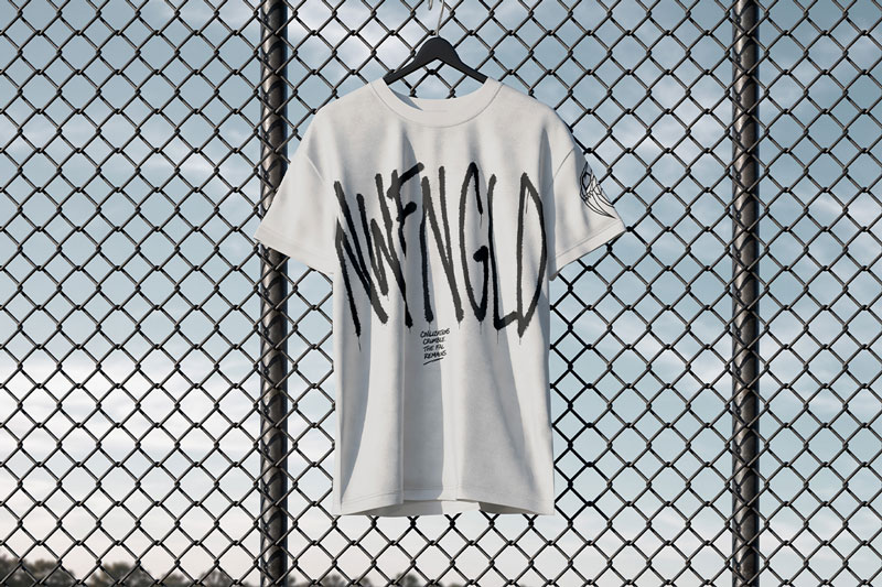 A white NWFNGLD graffiti-print t-shirt on a hanger clipped to a chain-link fence against a blue sky.